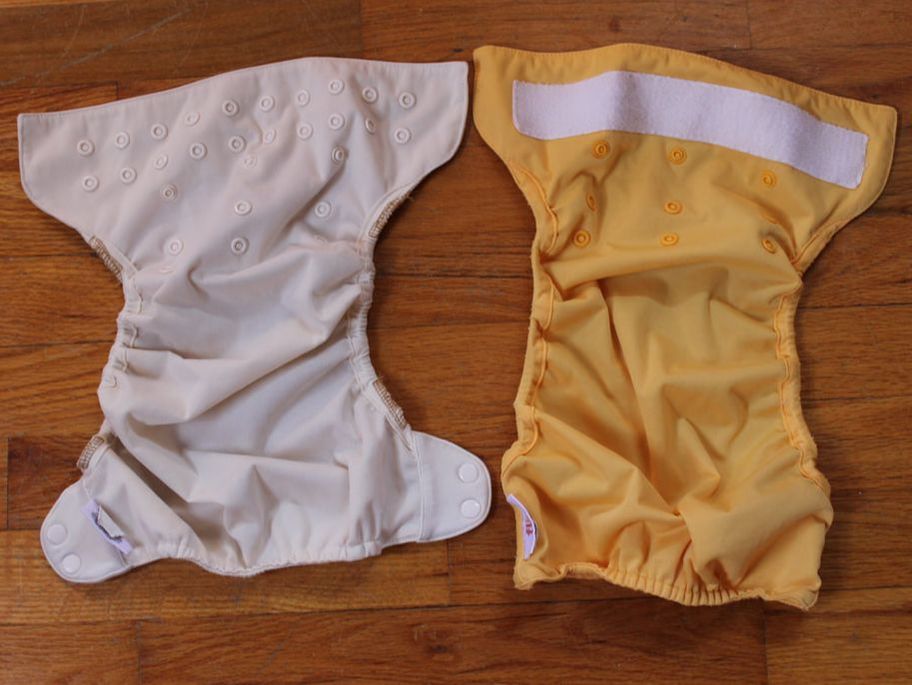 An off-white diaper next to a yellow diaper on a wood background. The off-white diaper is on the left, yellow on the right. The off-white diaper is about two inches shorter than the yellow diaper.